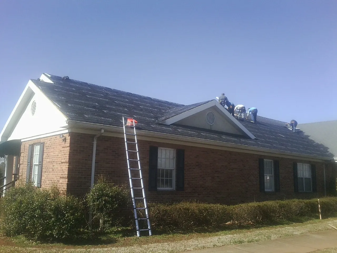 Crew tearing shingles off a brick ranch roof with a ladder set — Emergency Roof Repair work by our crew in Lexington